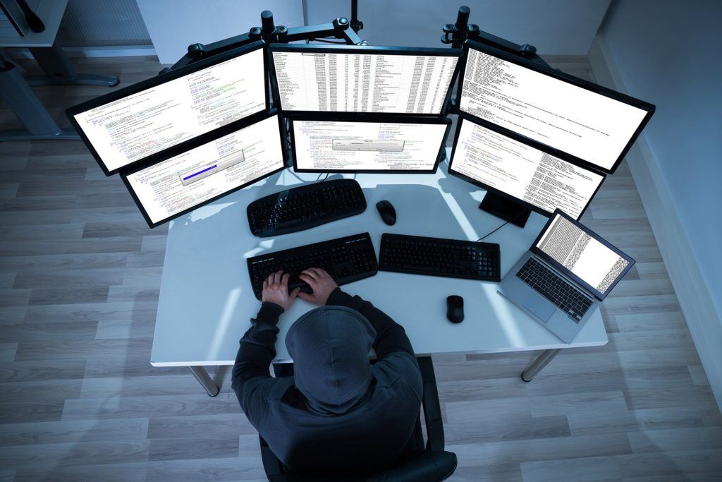 dark workspace with multiple screens for coding and data analysis. tips to ensure cyber security.