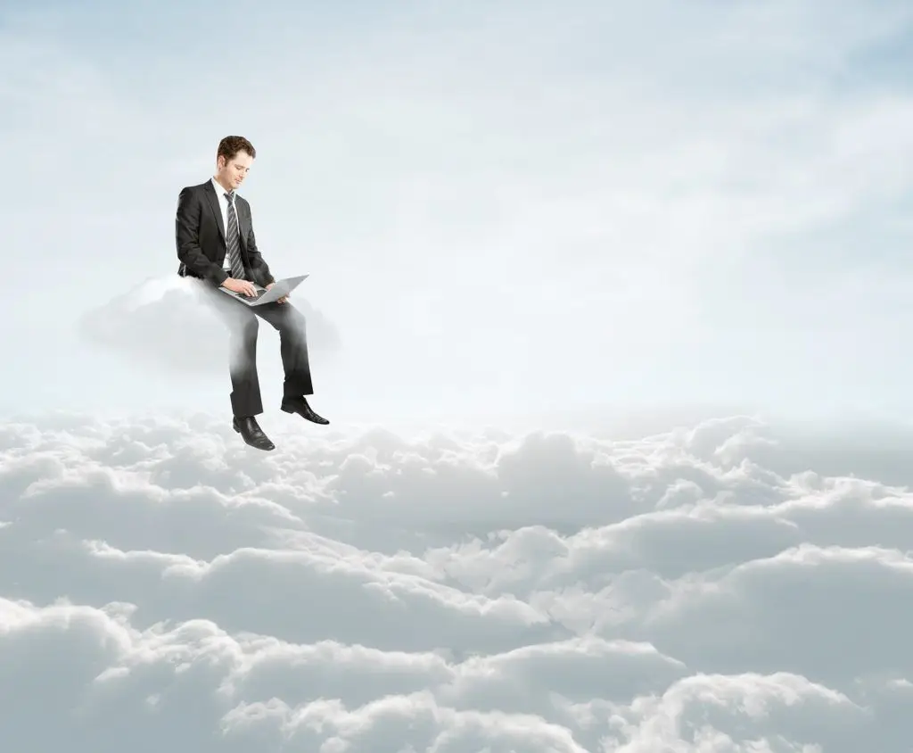 Innovative Productivity: Man In Suit Works On Laptop On Fluffy Cloud In Serene Sky. How Does The Cloud Help Businesses. innovative productivity: man in suit works on laptop on fluffy cloud in serene sky. how does the cloud help businesses.