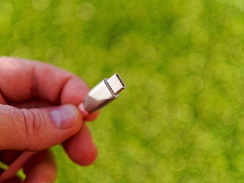 hand holding pink usb connector in nature, contrast with green background.