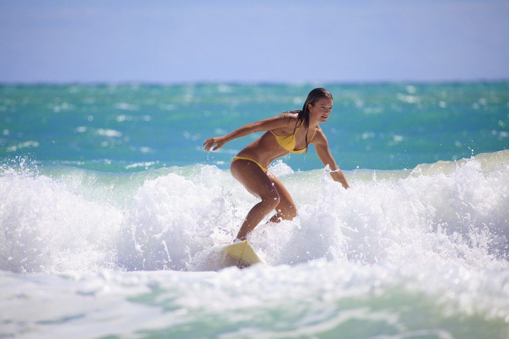 Surfer in yellow bikini riding vibrant turquoise waves, embodying summer adventure. distracting websites.