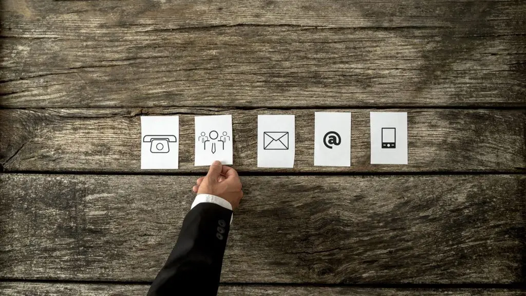hand selecting modern communication icons on rustic wooden table: camera, silhouettes, envelope, @ symbol, smartphone. managed services.