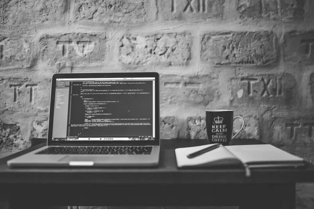 minimalist workspace with laptop displaying code, stone wall background, notebook, pen, and coffee mug. update.
