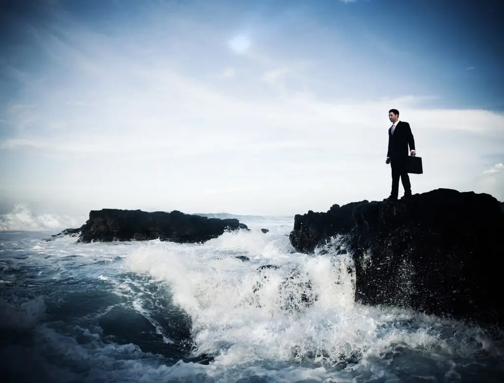 resilient man in black suit stands on rocky outcrop, facing powerful ocean waves. optimal it.