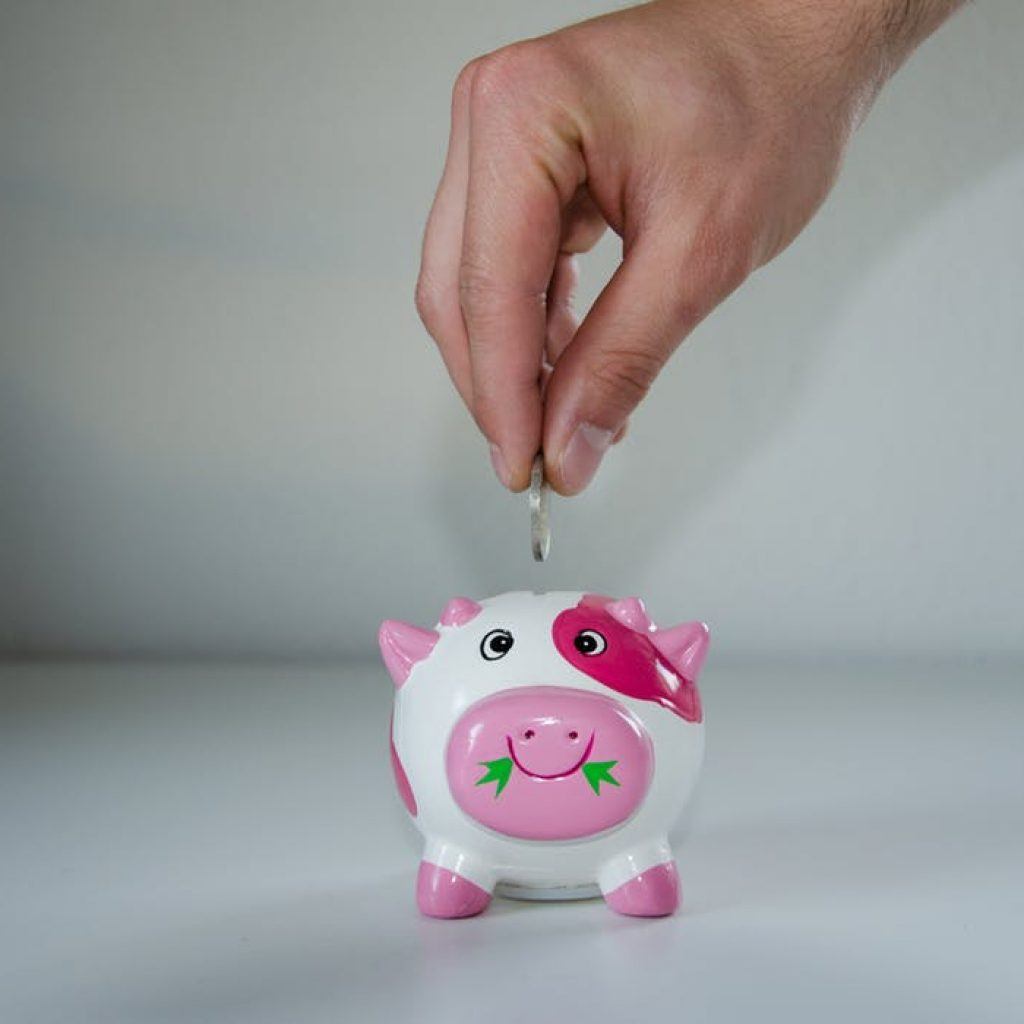 hand inserting coin into whimsical piggy bank, symbolizing joyful saving. security.