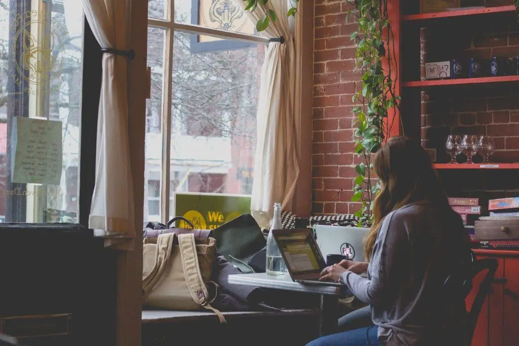 tranquil urban café scene with woman working on laptop, surrounded by natural light and greenery. windows.