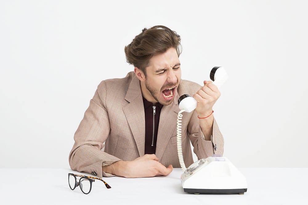 young man in beige blazer with intense emotions on vintage phone at white table.