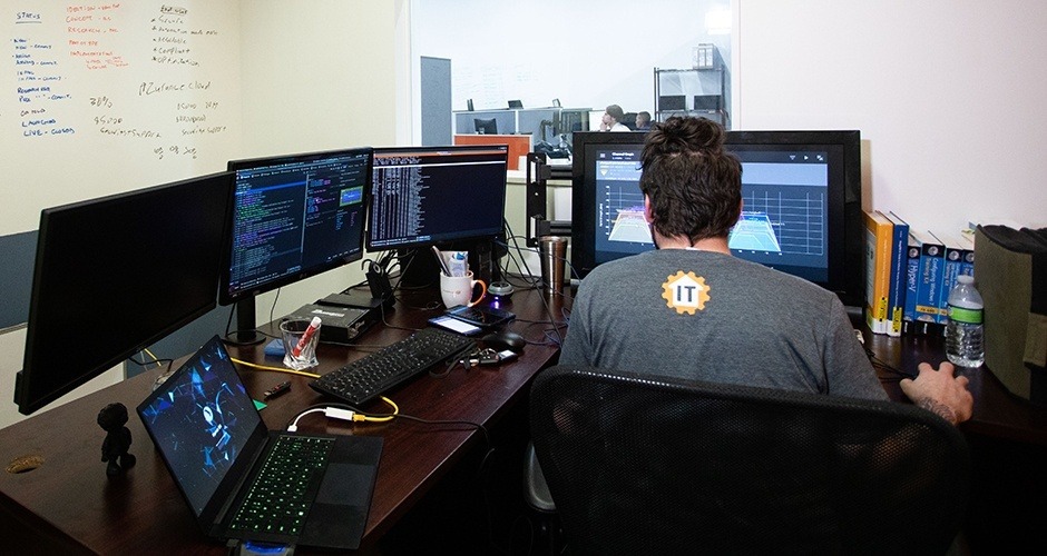 a man sitting at a desk in front of three computer monitors