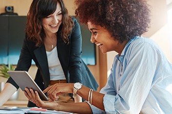 two women sitting at a table looking at a tablet