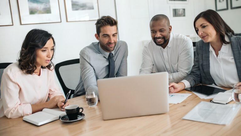 three people sitting at a table looking at a laptop