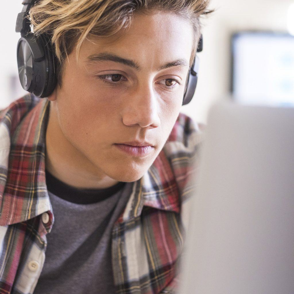 a young man wearing headphones looking at a laptop