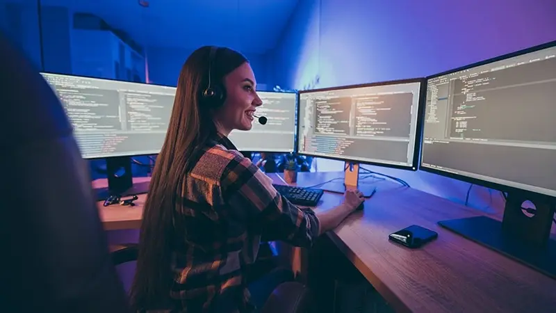 a woman sitting in front of two computer monitors