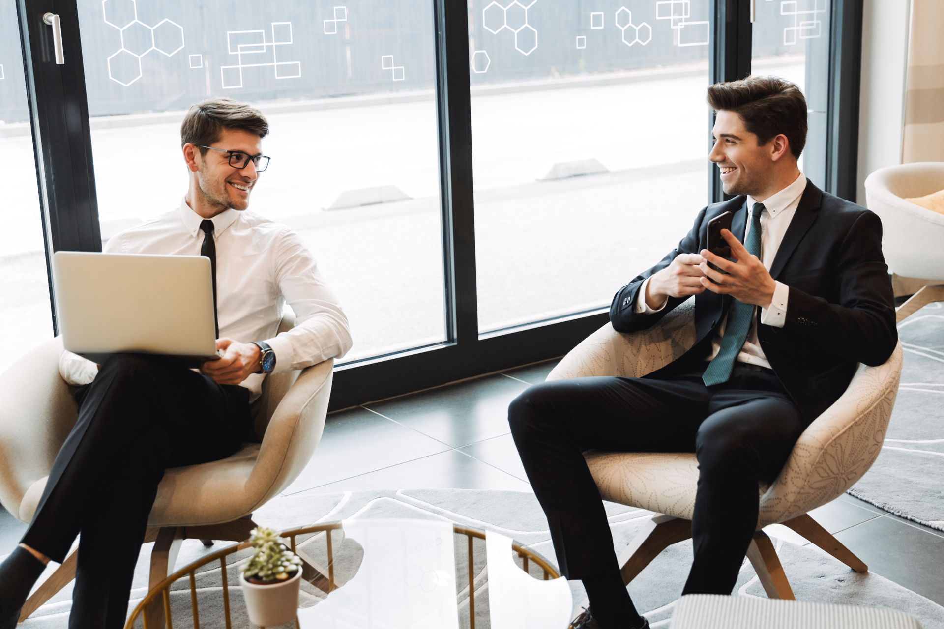 two men sitting in chairs with laptops