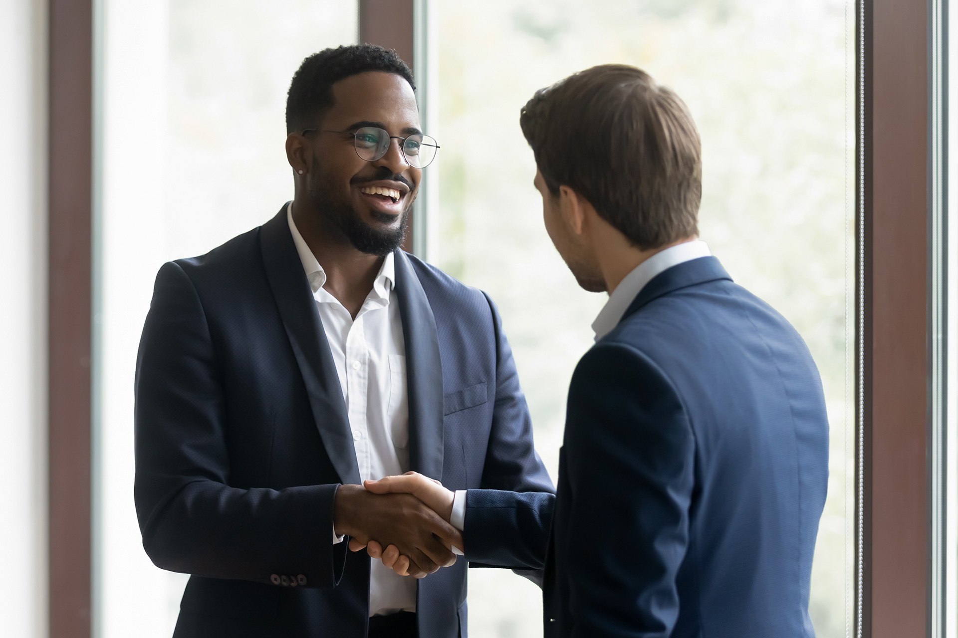 two men shaking hands in front of a window