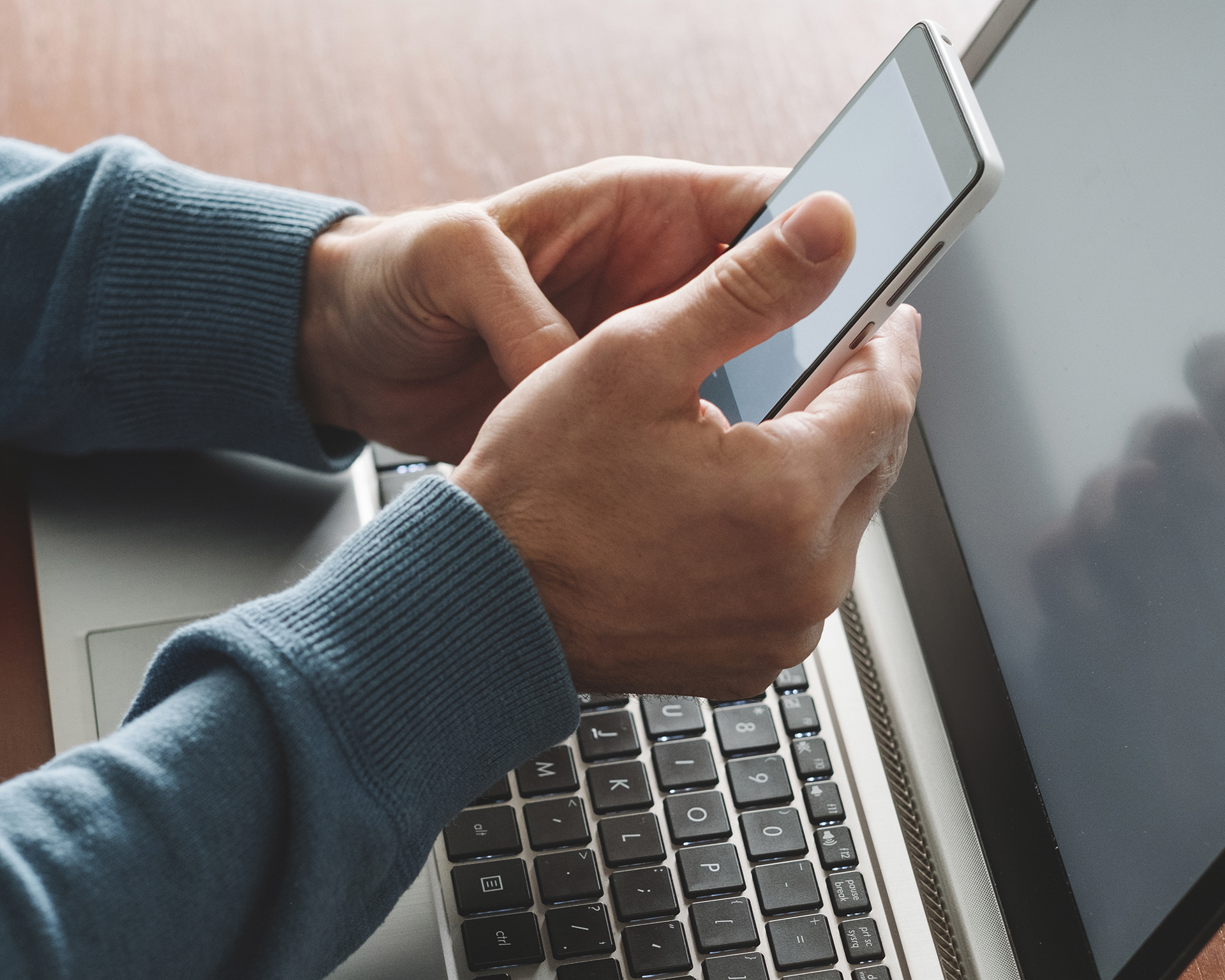 a person using a cell phone while sitting at a laptop