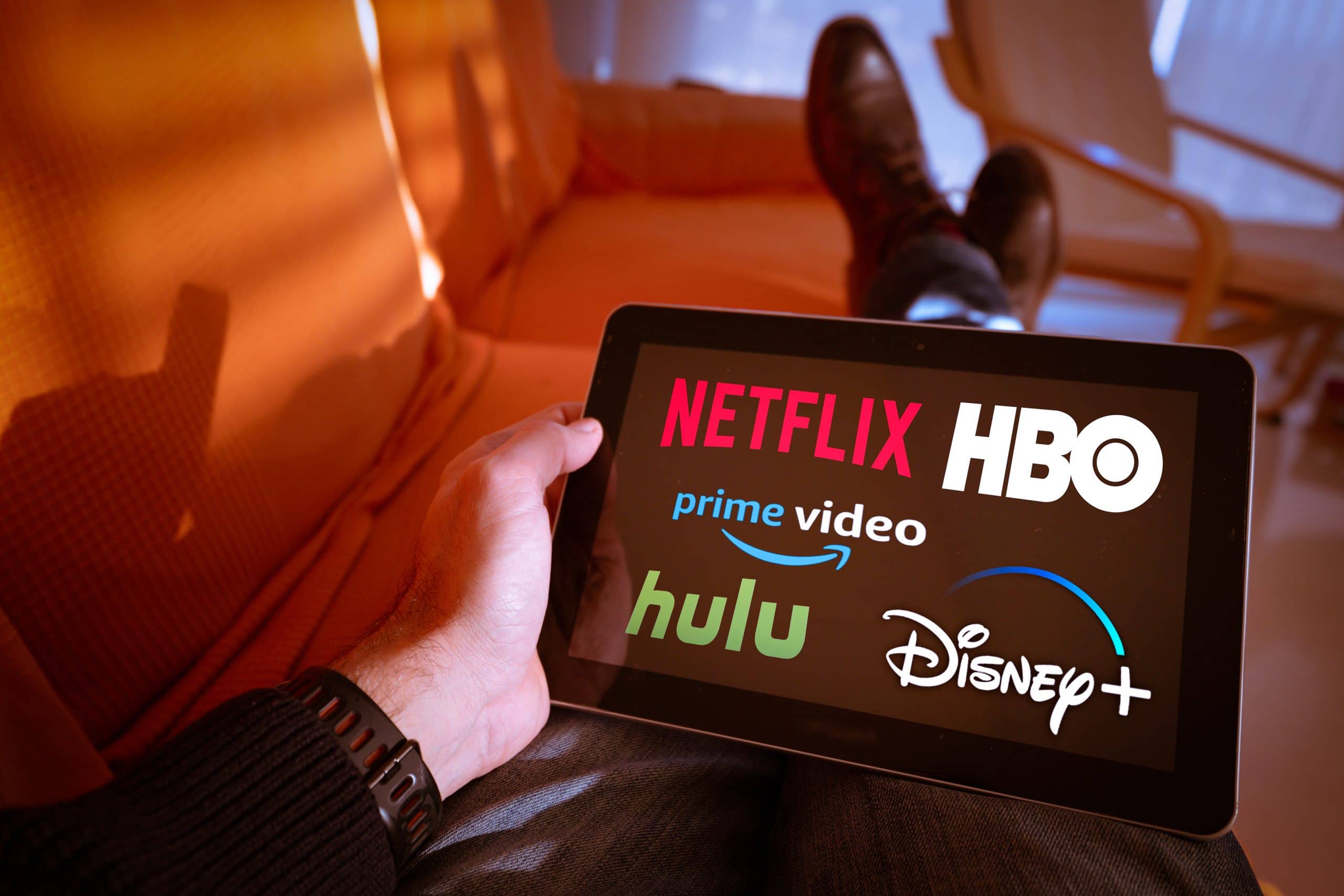 Cozy home entertainment: Popular streaming services logos on tablet, relaxing on orange couch.