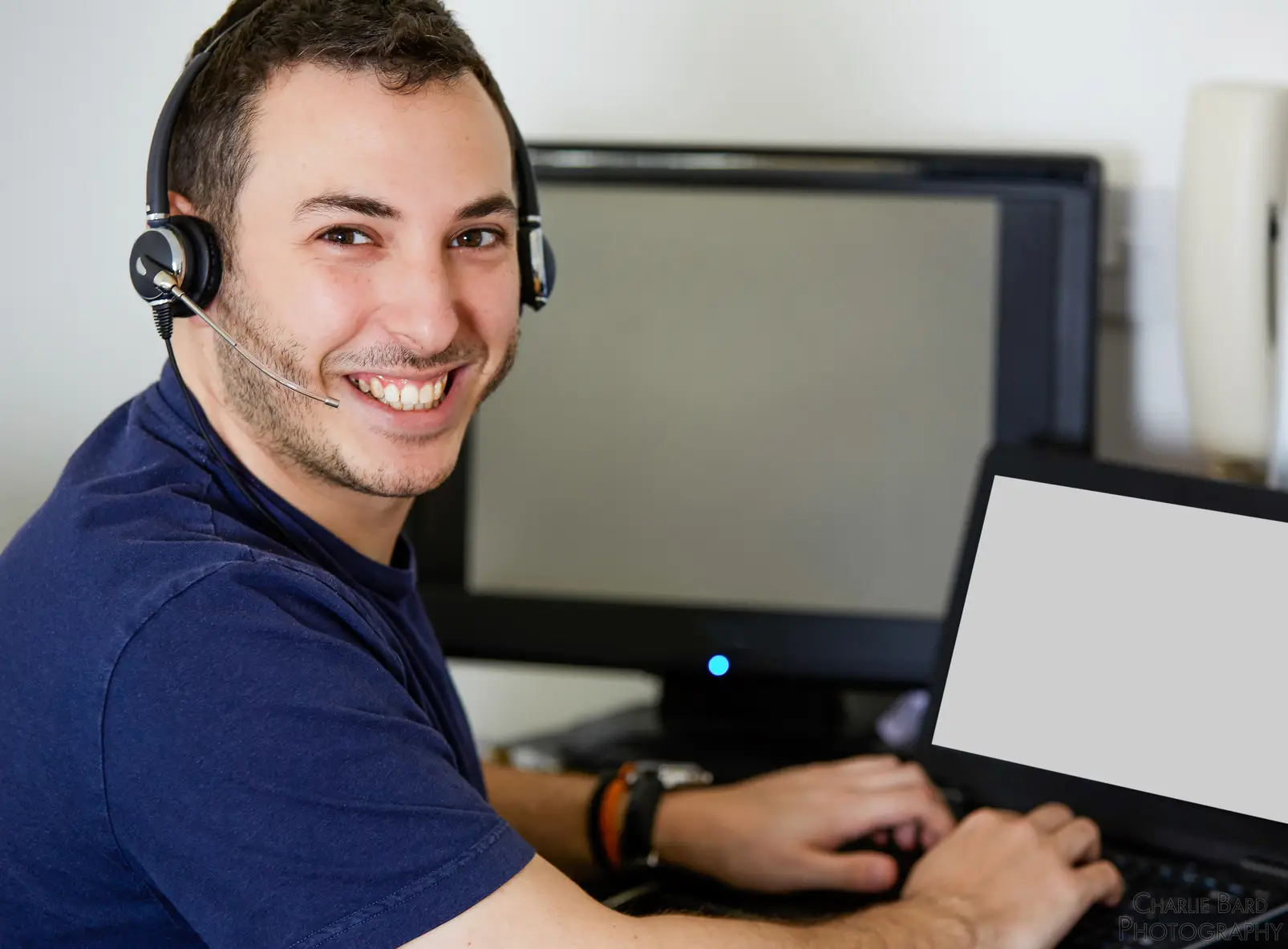 Happy man in home office working on laptop with headset, modern and productive environment.