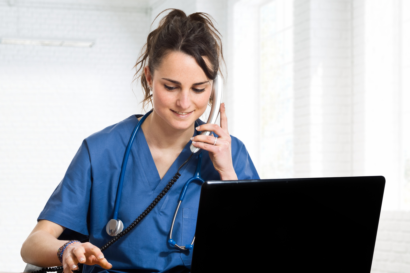 a woman in scrubs is talking on the phone while using a laptop