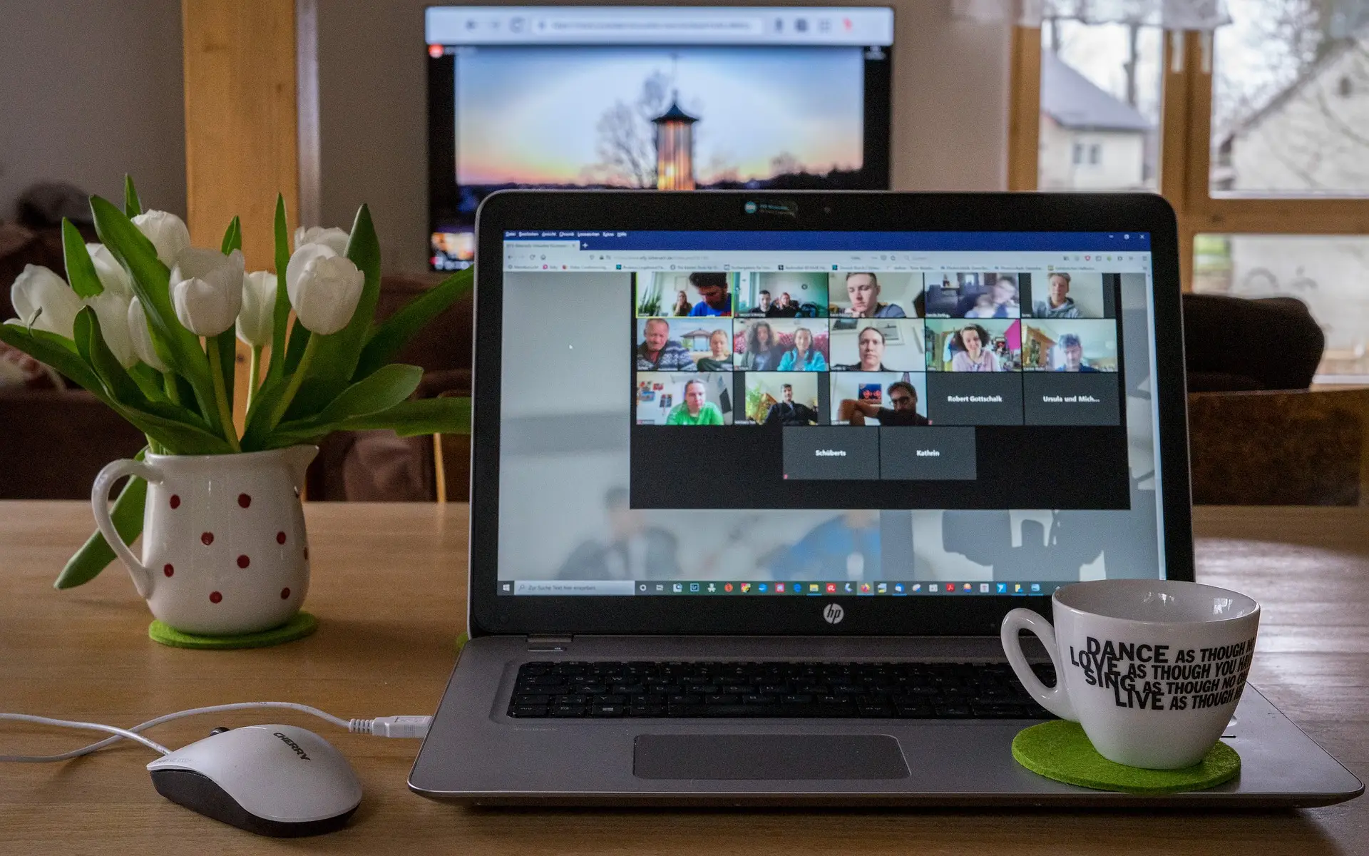 Sunset-themed home office with video call, tulips, coffee mug, and motivational message.
