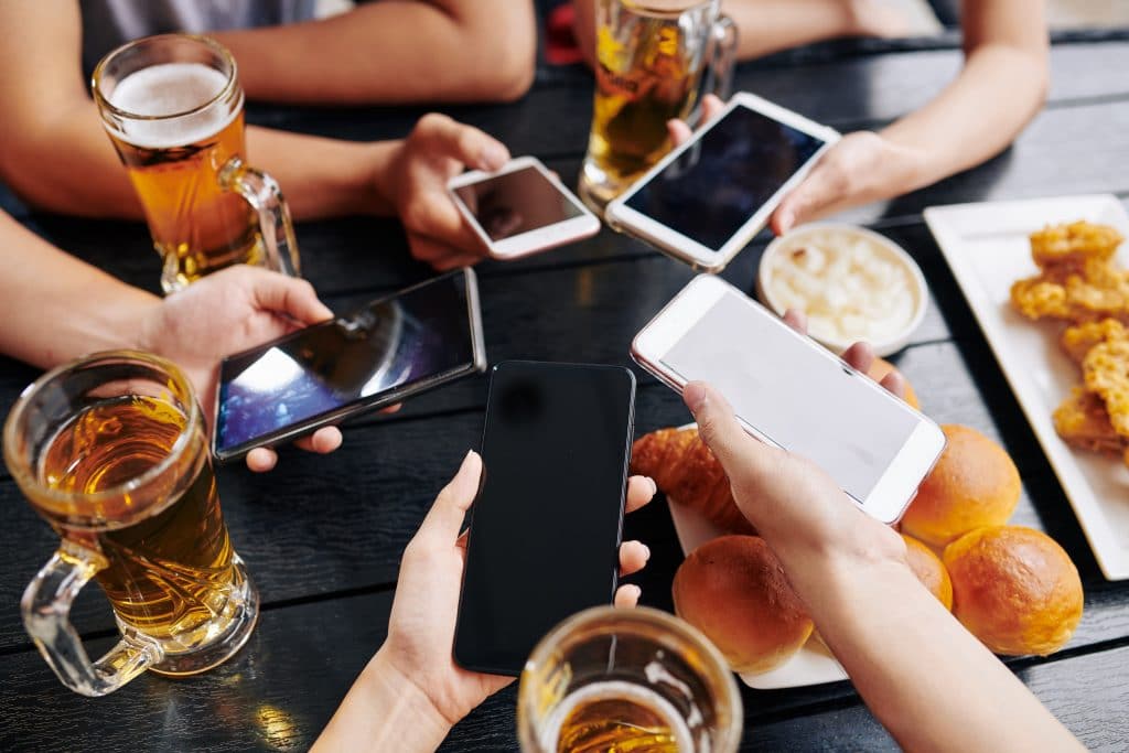 friends socializing with smartphones, beer, and food at a lively gathering.