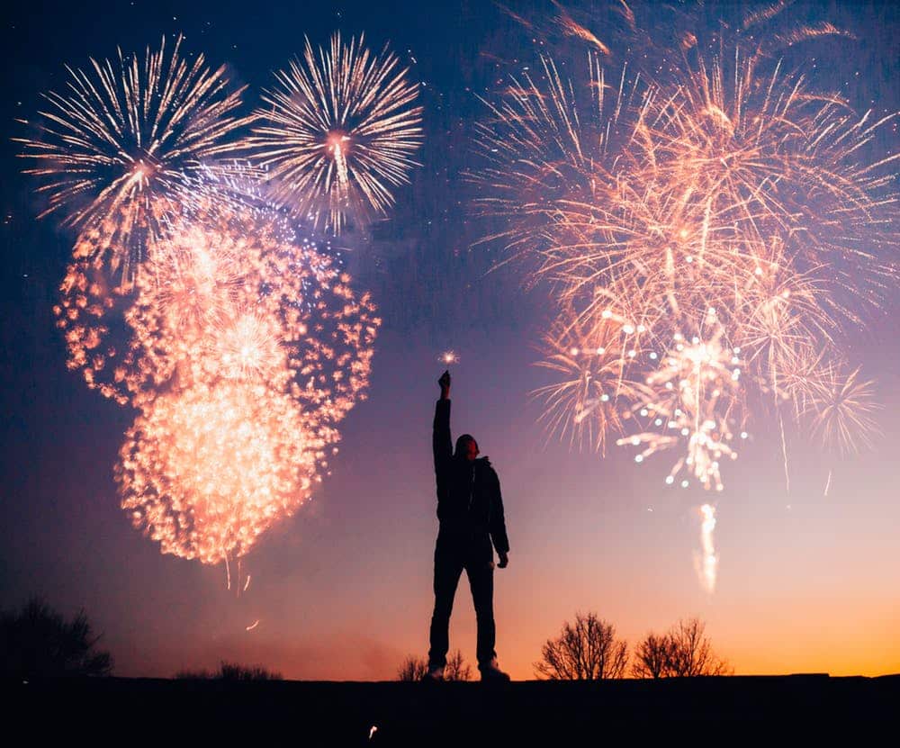 a person standing on a hill with fireworks in the sky