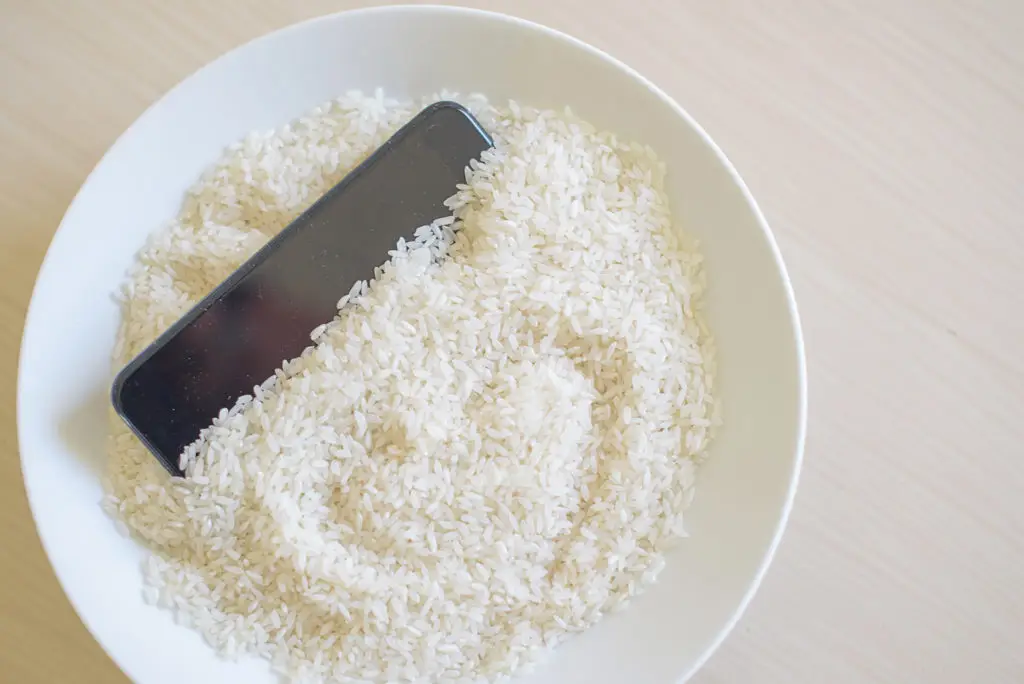 Modern Technology Meets Tradition: Smartphone Nestled In Bowl Of Uncooked White Rice. Smartphone Gets Wet modern technology meets tradition: smartphone nestled in bowl of uncooked white rice. smartphone gets wet