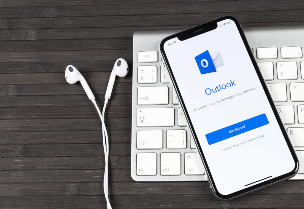 efficient workspace with outlook app, phone, keyboard, and earbuds for productivity.