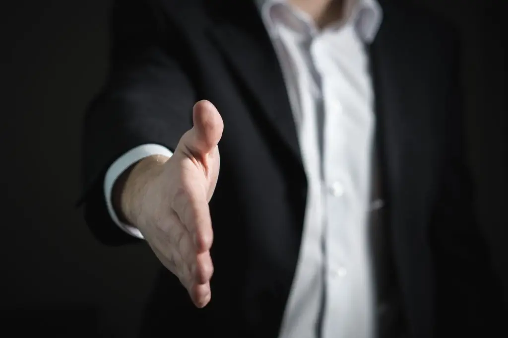 Business Professional Extending A Handshake In A Formal Setting For Agreement And Welcome. business professional extending a handshake in a formal setting for agreement and welcome.
