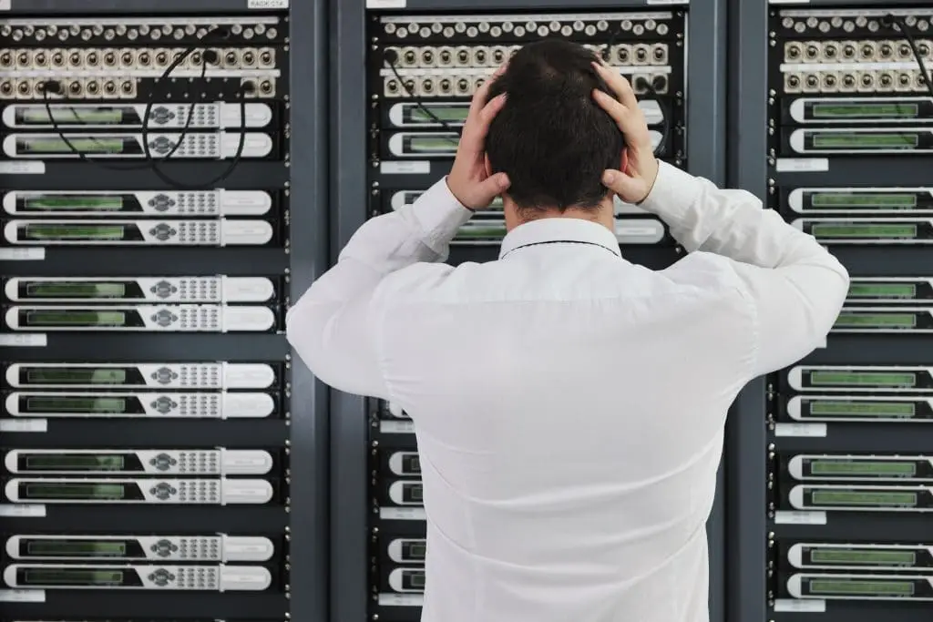 frustrated it worker overwhelmed by complex server equipment in dimly lit room. offsite backup.