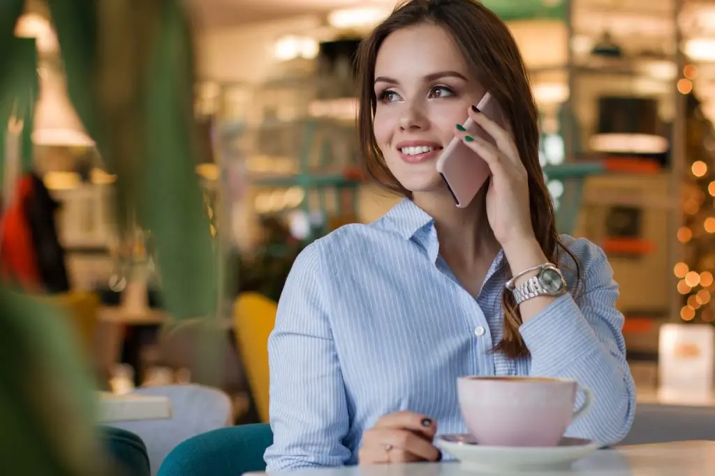 Serene Woman Enjoying Phone Call In Cozy Café With Pink Teacup. serene woman enjoying phone call in cozy café with pink teacup.