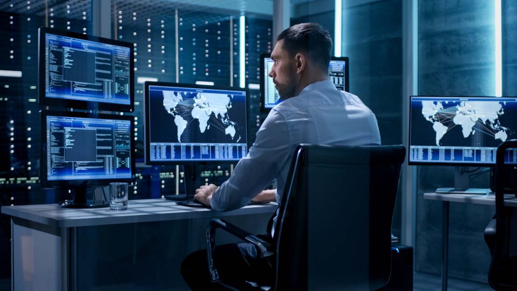 a man sitting at a desk in front of multiple monitors