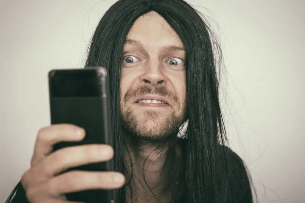 Surprised Man With Long Hair Reacting To Smartphone Content. surprised man with long hair reacting to smartphone content.