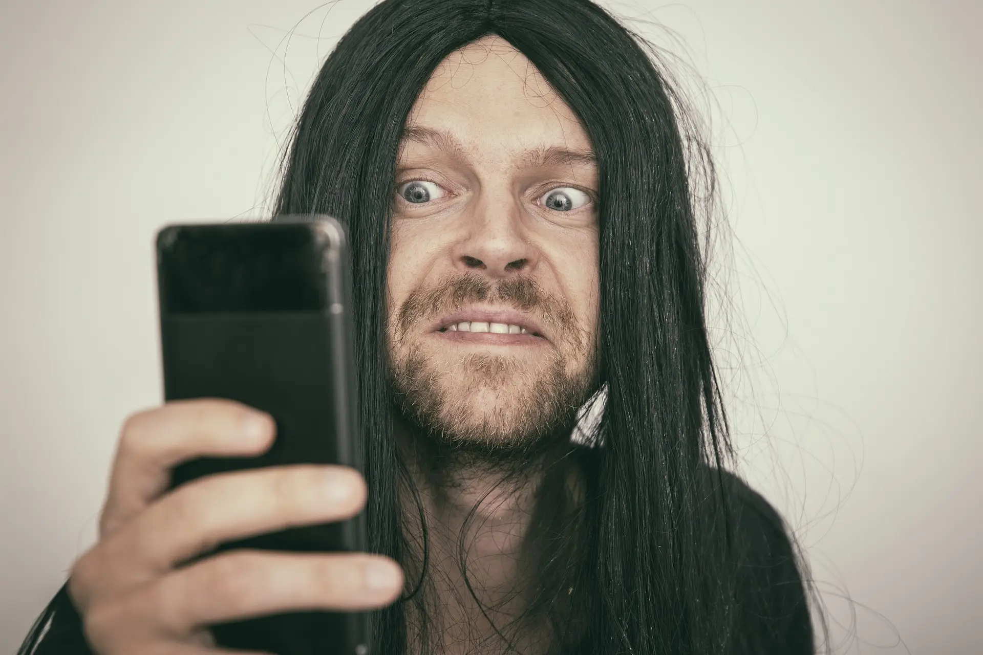 Surprised man with long hair reacting to smartphone content.
