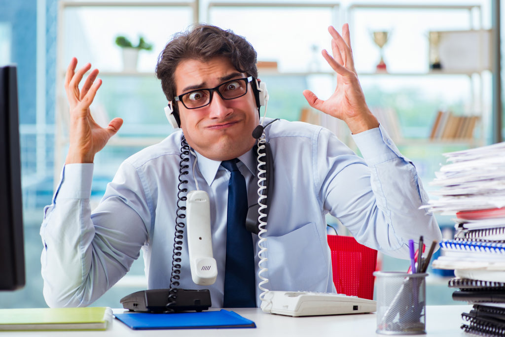 stressed man in cluttered office dealing with frustrating phone call.