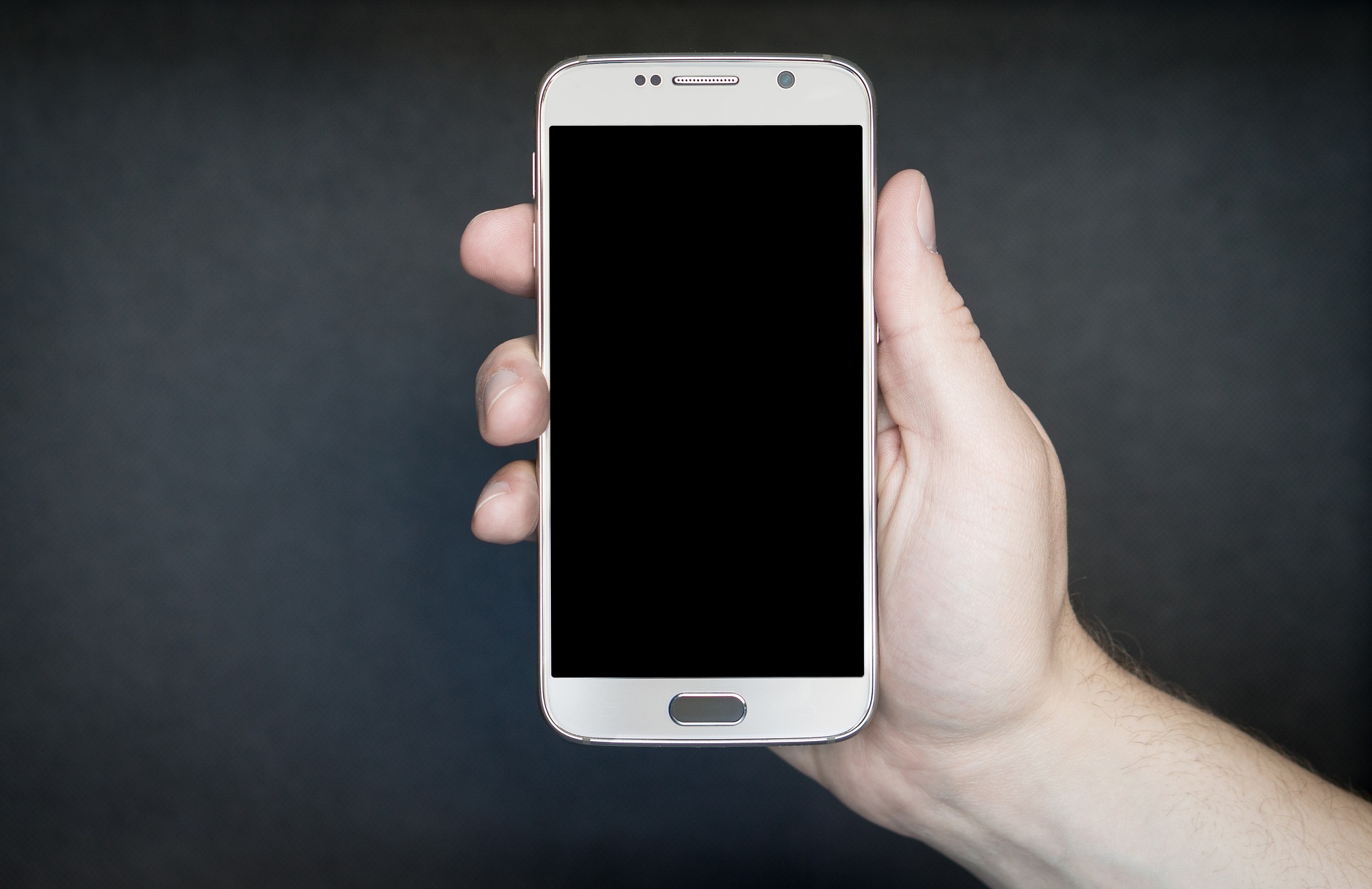 a hand holding a white cell phone with a black screen