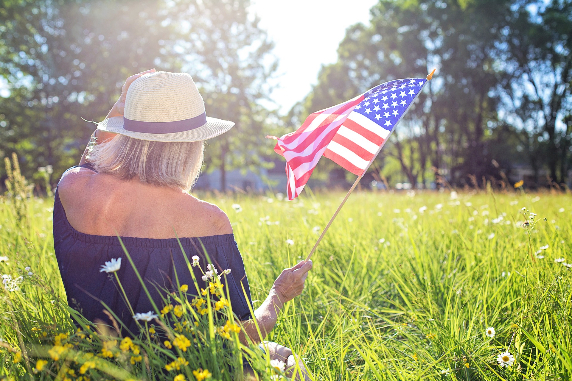 a woman sitting in the grass holding an american flag