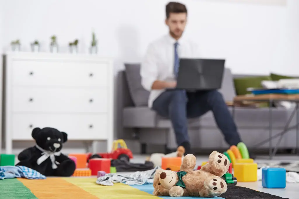 Modern Family Home: Father Works On Laptop Surrounded By Kids Toys. Telecommuting. modern family home: father works on laptop surrounded by kids toys. telecommuting.