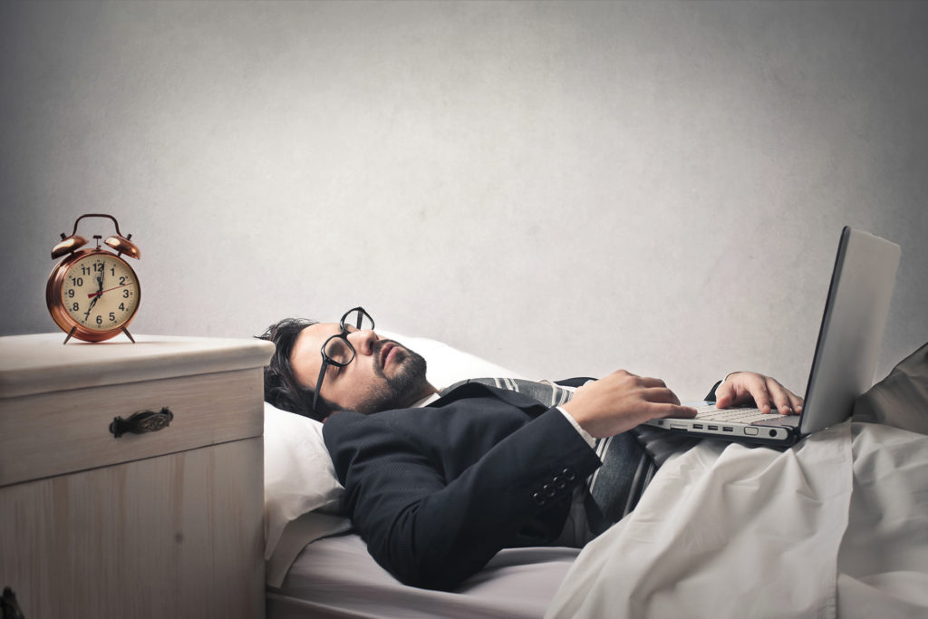 man in suit resting with laptop and alarm clock, balancing work and relaxation.