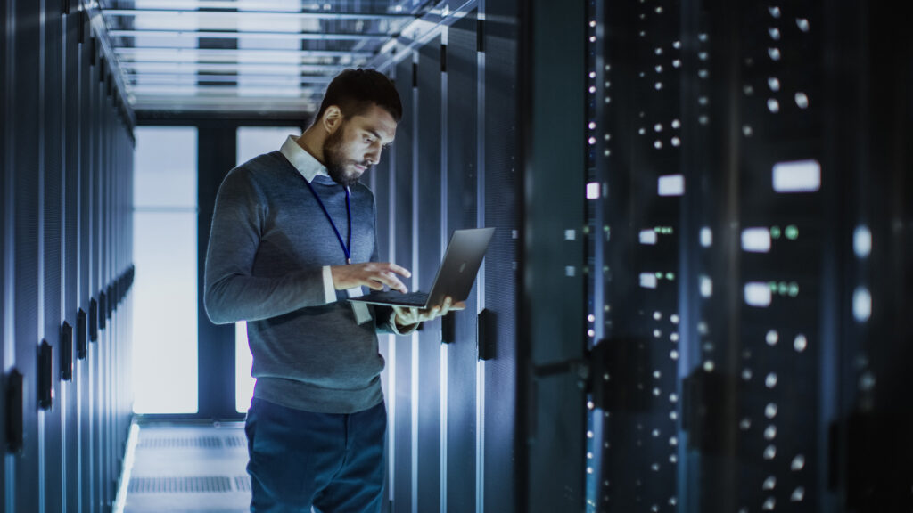 a man standing in a server room using a laptop