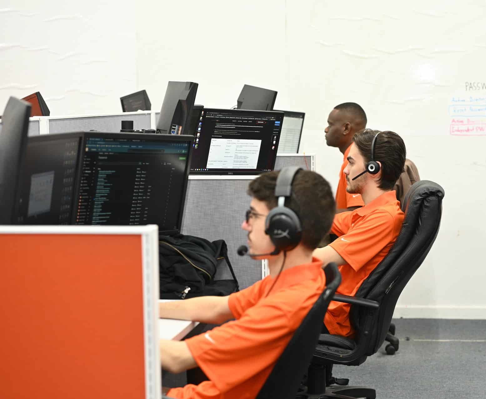three men in orange shirts sitting at computers
