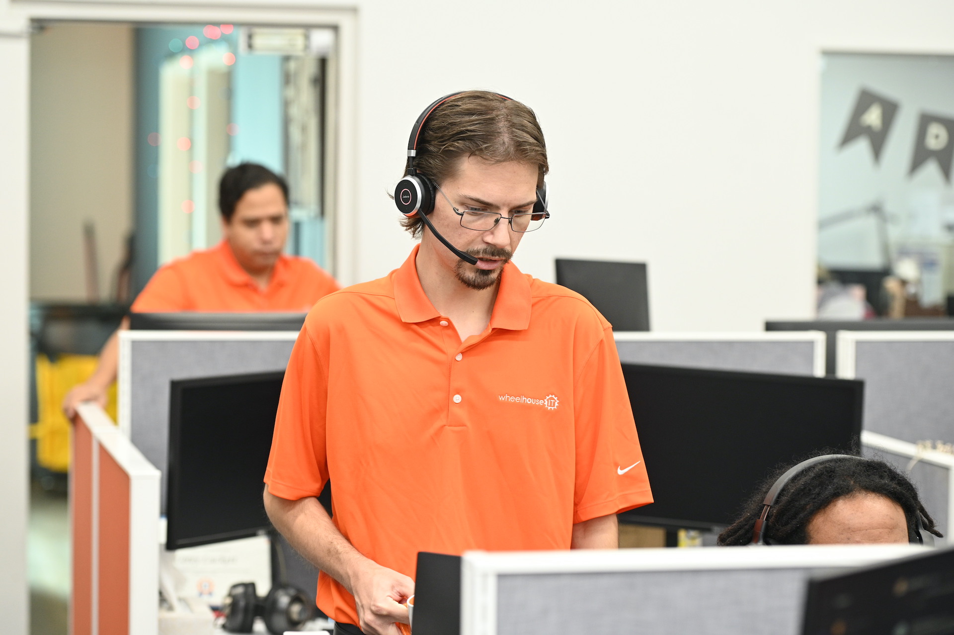 two men in orange shirts are working on computers