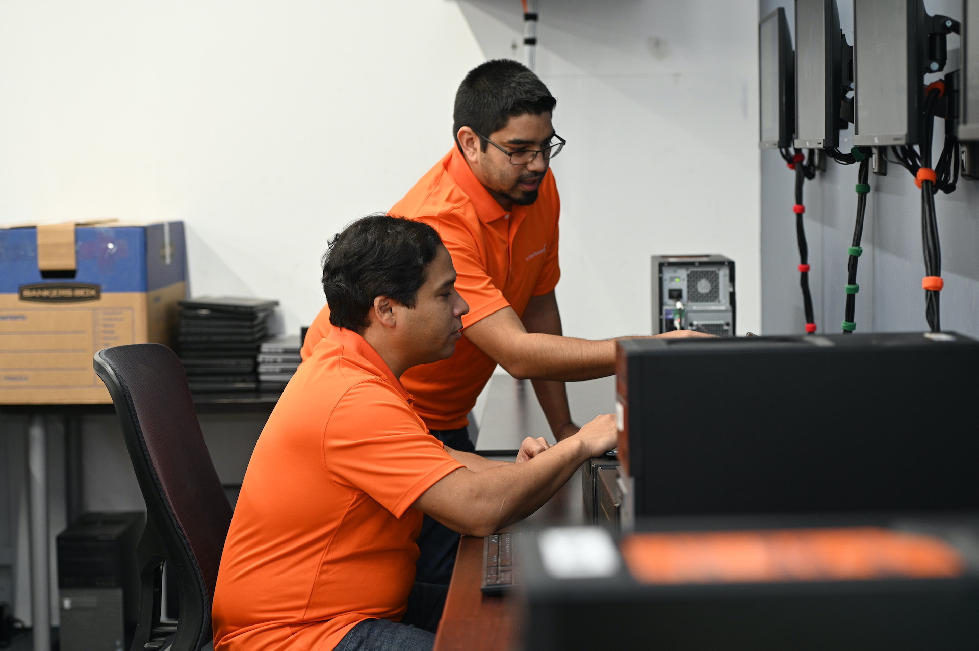 two men in orange shirts working on a computer