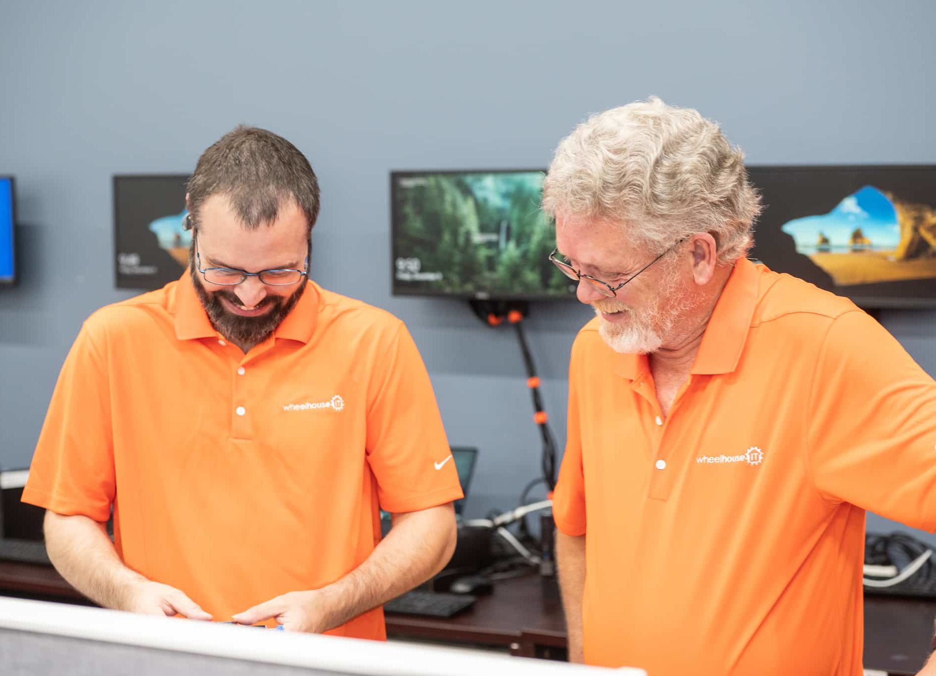 two men in orange shirts looking at a laptop