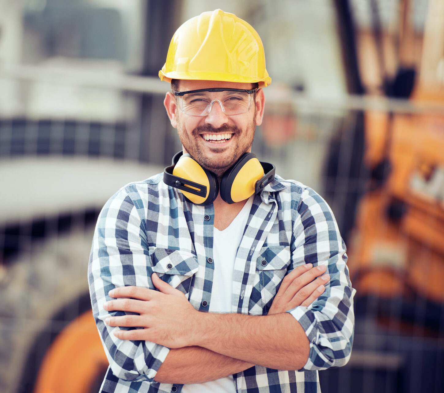 a construction worker wearing ear muffs standing in front of a bulldozer