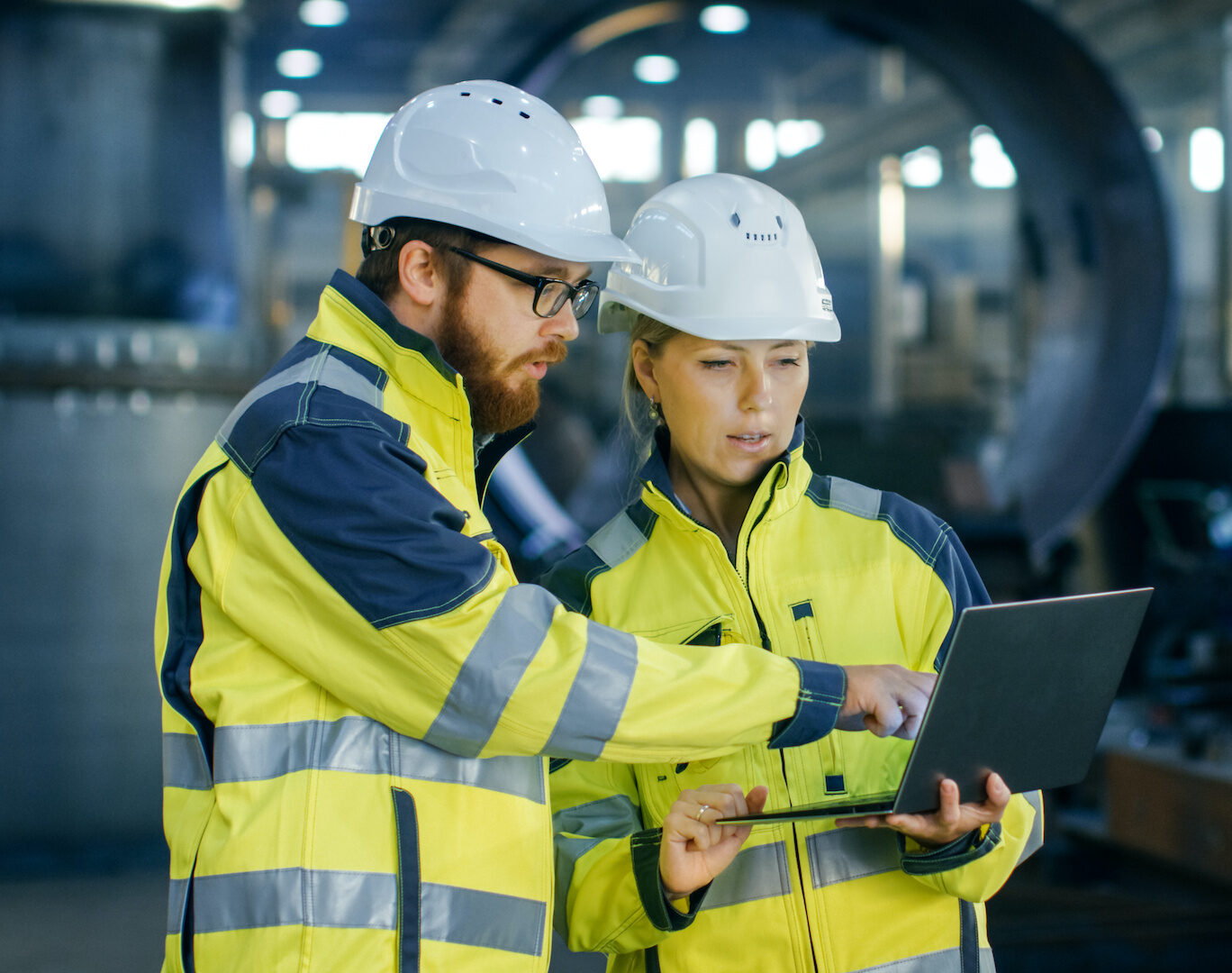 two people in hard hats are looking at a laptop