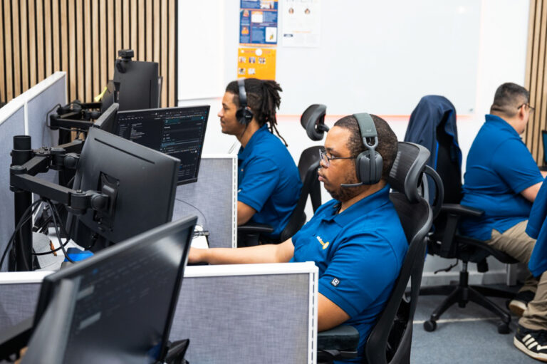 three men in blue shirts sitting at computers