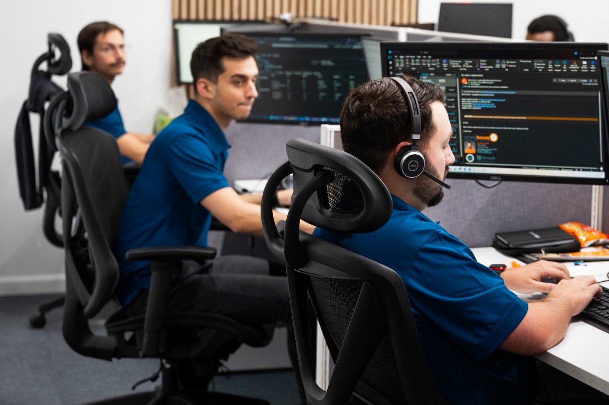 two men sitting in front of computer monitors wearing headphones