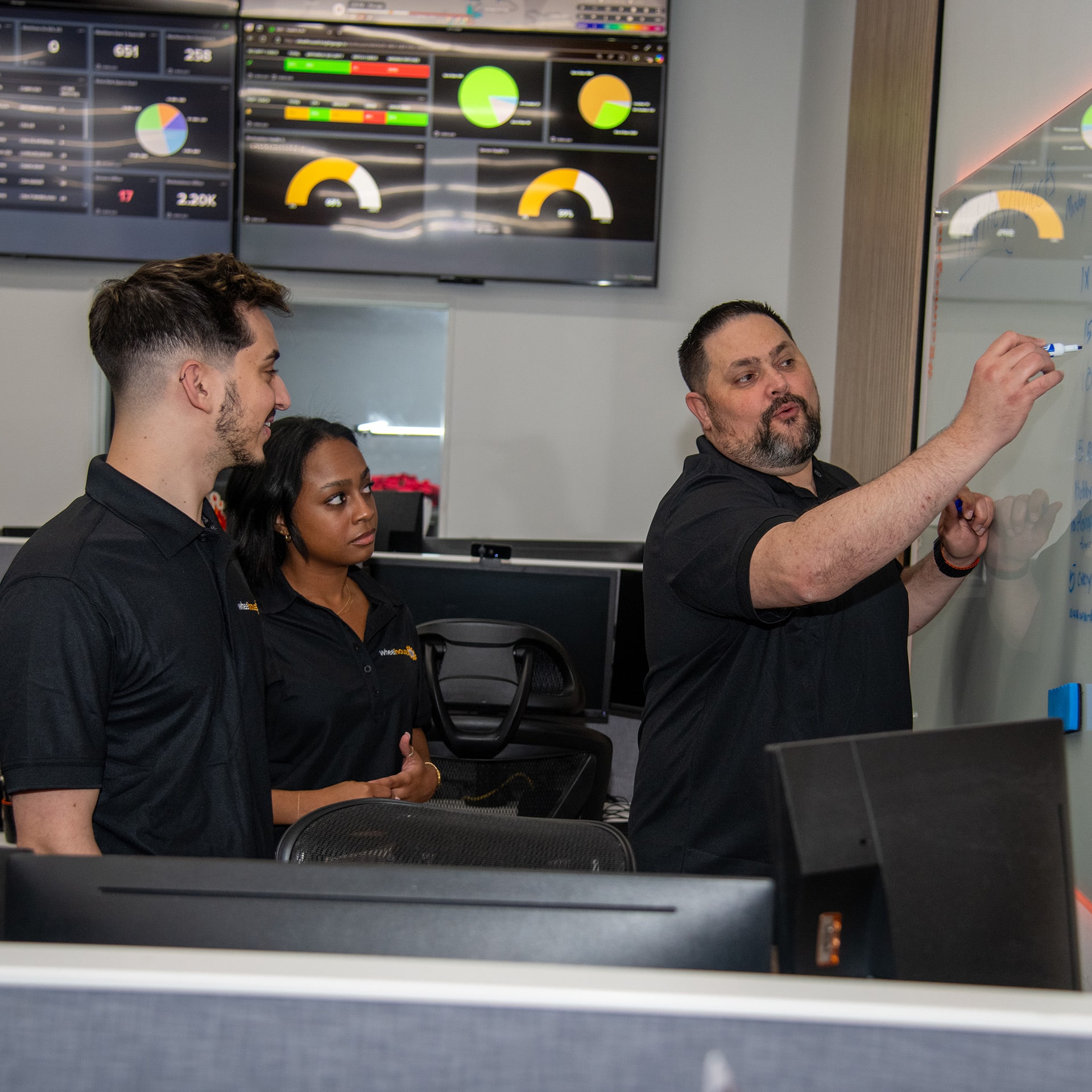 collaborative team discussion in modern tech office setting with whiteboard and monitors.