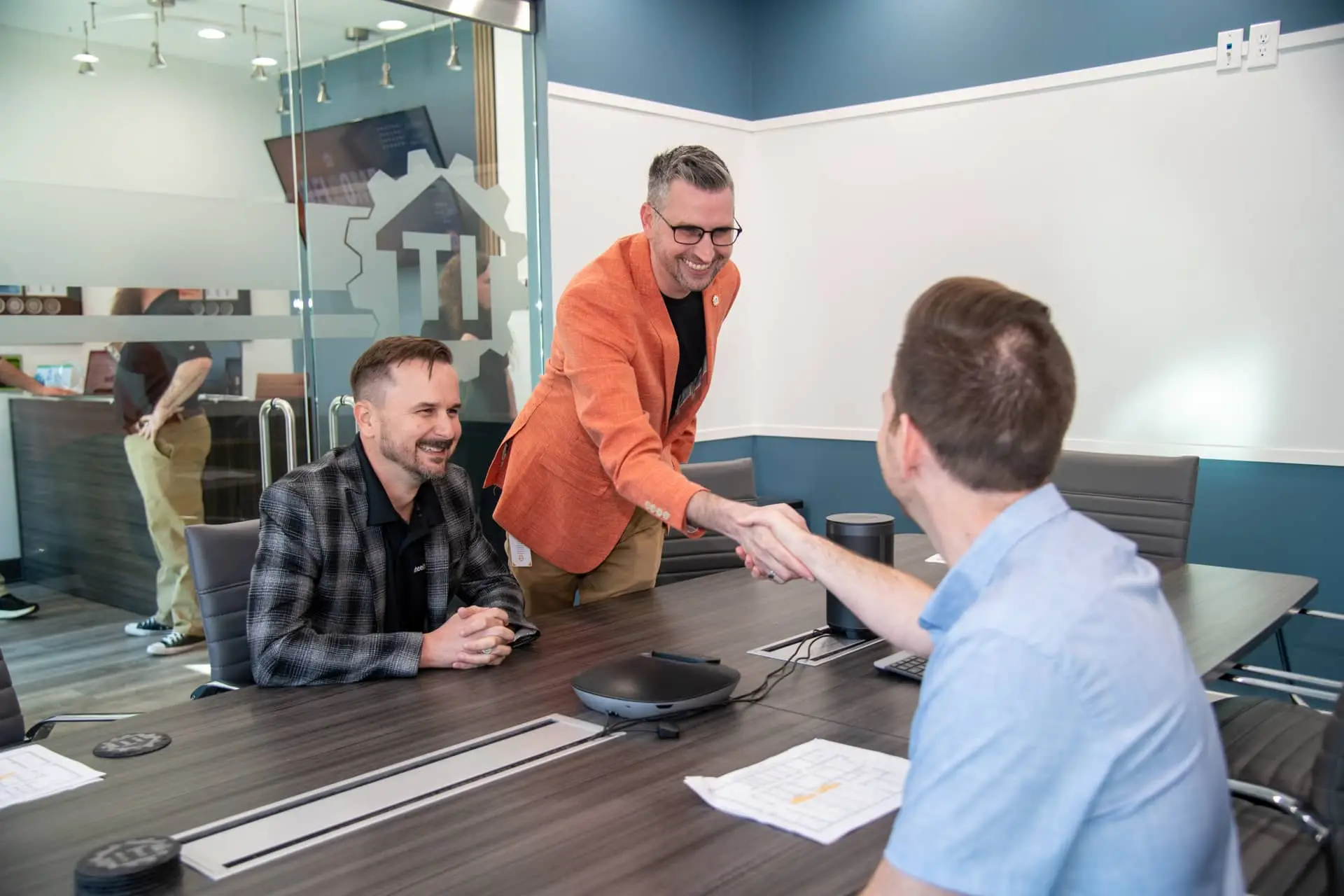 professionals shake hands during a co-managed it services meeting in a modern conference room.