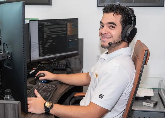cloud managed services expert smiling at a multi-monitor workstation with a headset.