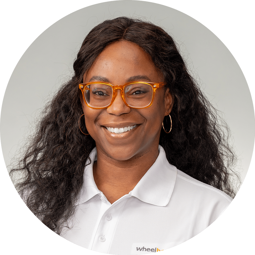friendly woman with orange glasses and white polo shirt featuring wheelhouse logo, smiling confidently.